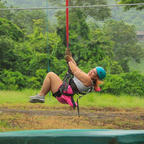 Person zip-lining in forest with blue helmet and pink outfit