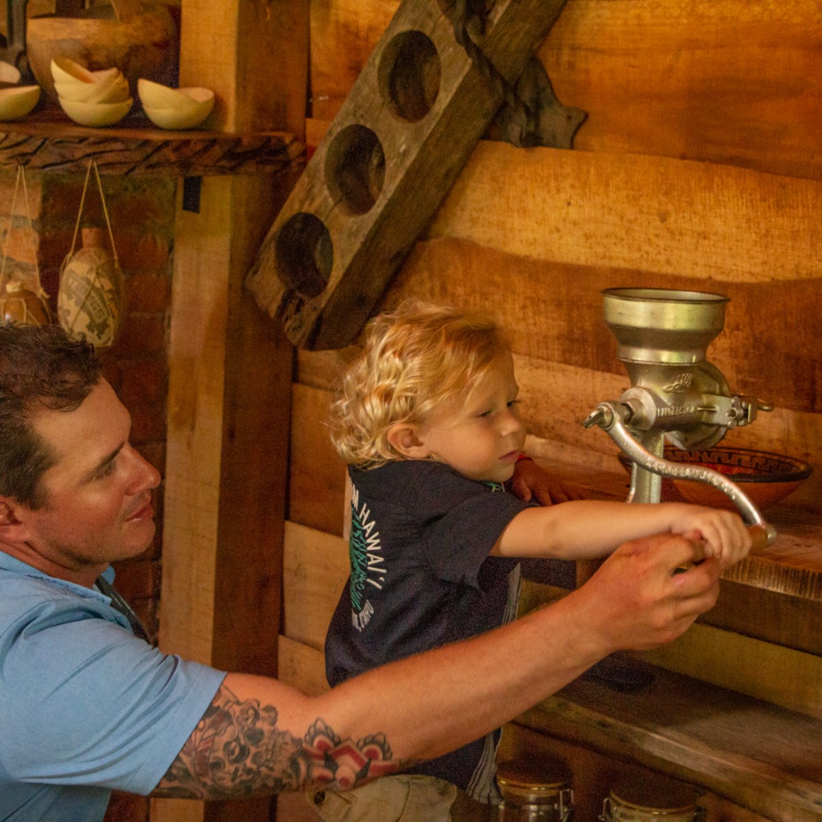 Adult assists child in using a manual grain mill on a wooden counter.