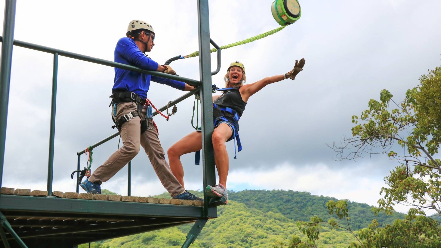 Woman bungee jumping from a platform assisted by a guide on a cloudy day.