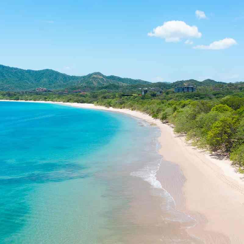 Aerial view of a tranquil beach with turquoise water and lush green hills in the background.