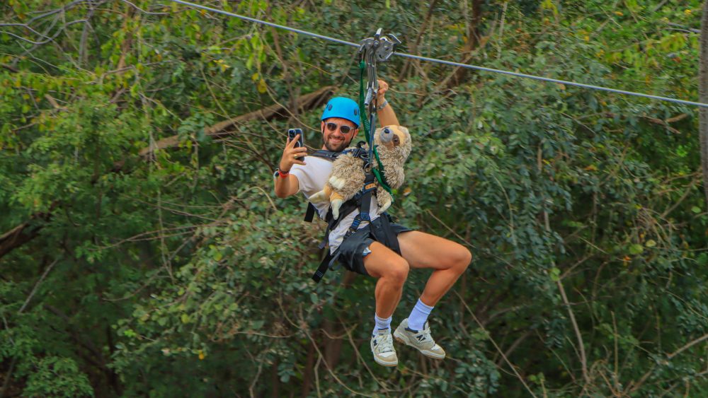 Person ziplining with a stuffed animal, taking a selfie.